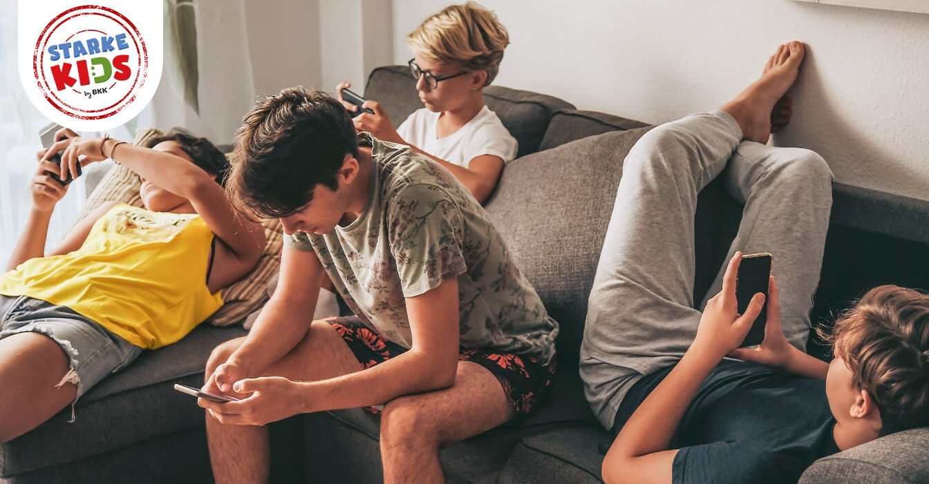 Eine Gruppe von Jugendlichen sitzt zusammen auf einem Sofa, jeder vertieft in sein eigenes Smartphone, ohne miteinander zu interagieren.